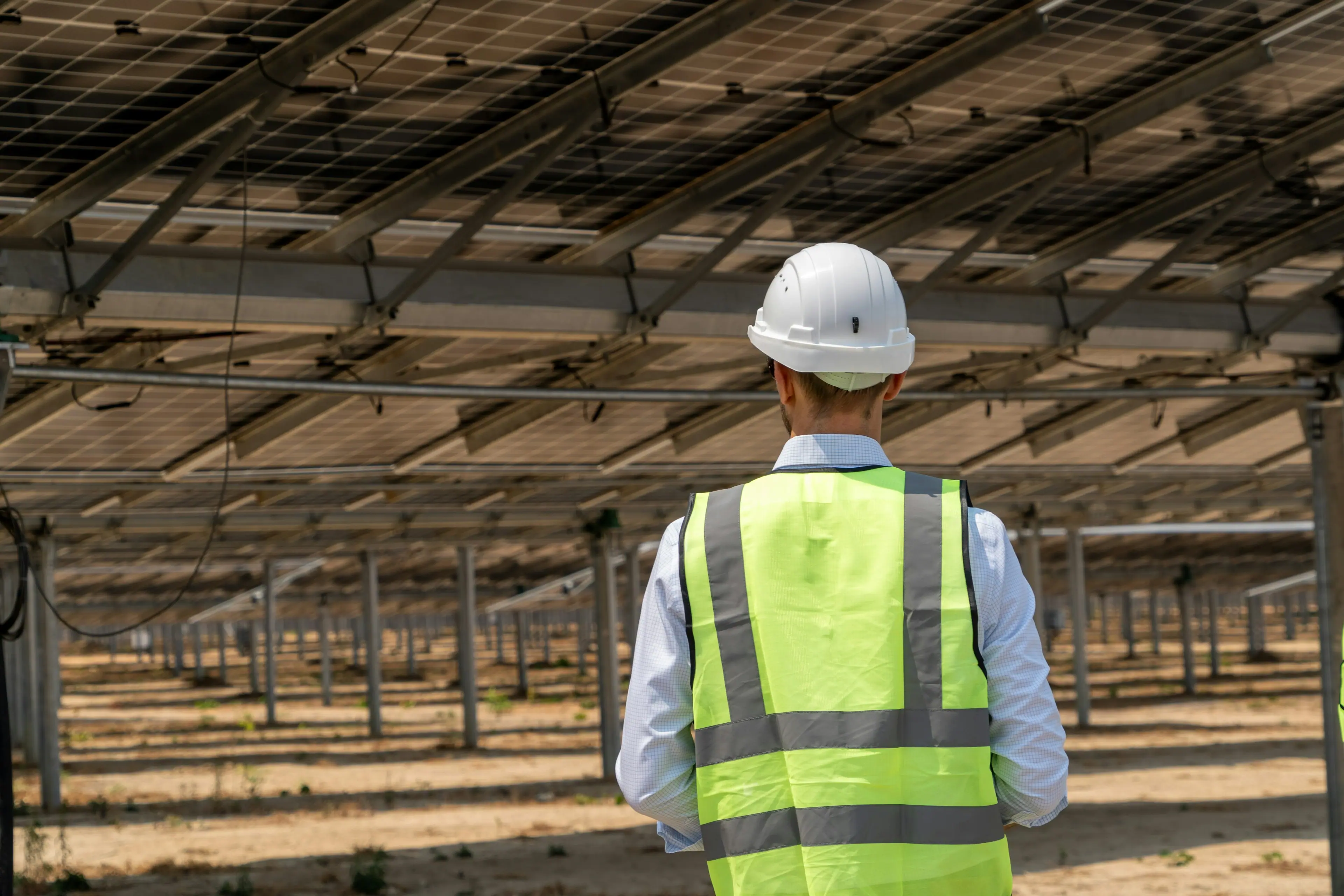 Solar engineer in a hard hat and safety vest inspecting a solar array