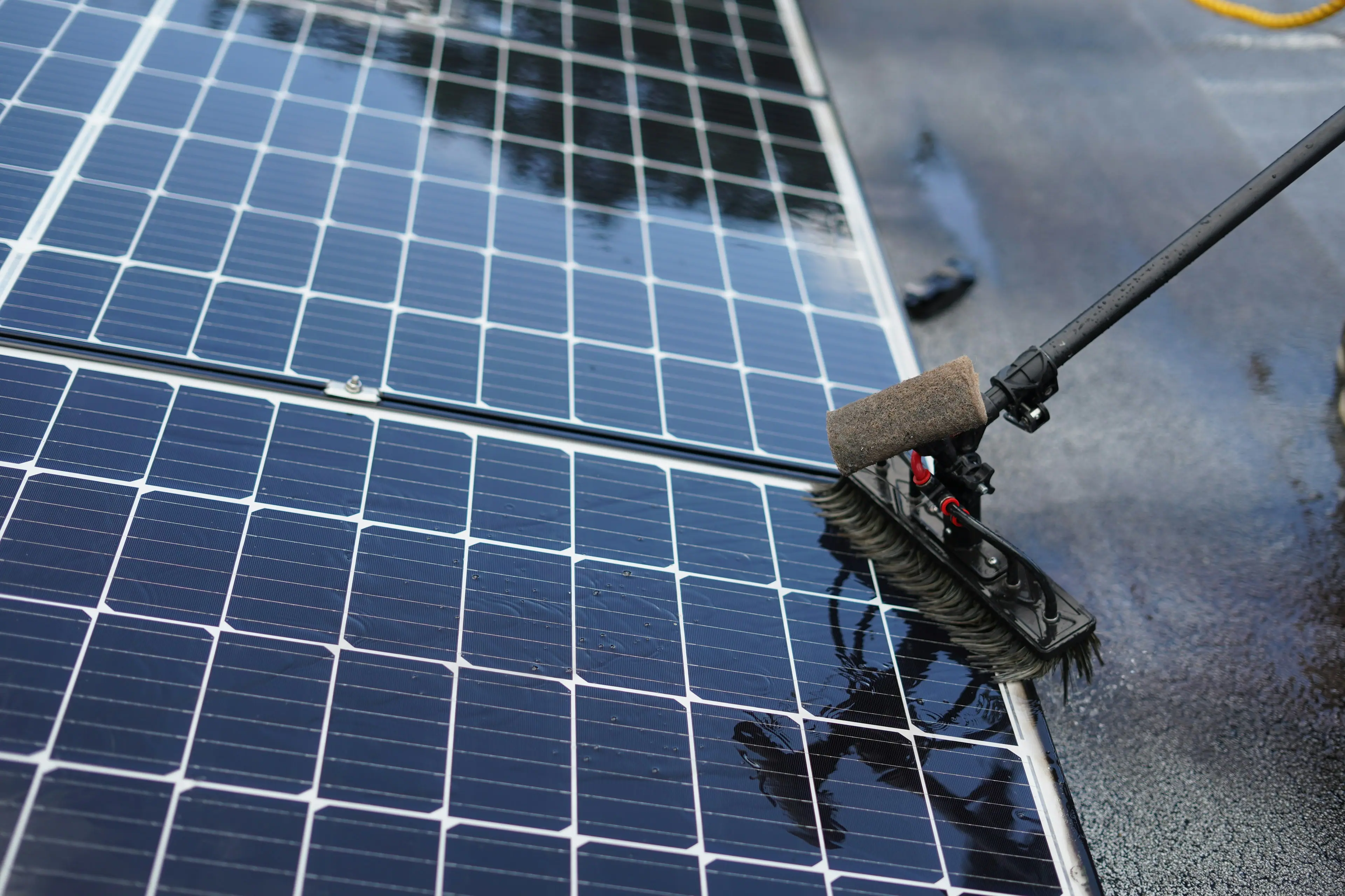 Technician cleaning dusty solar panels with a soft long-handled brush